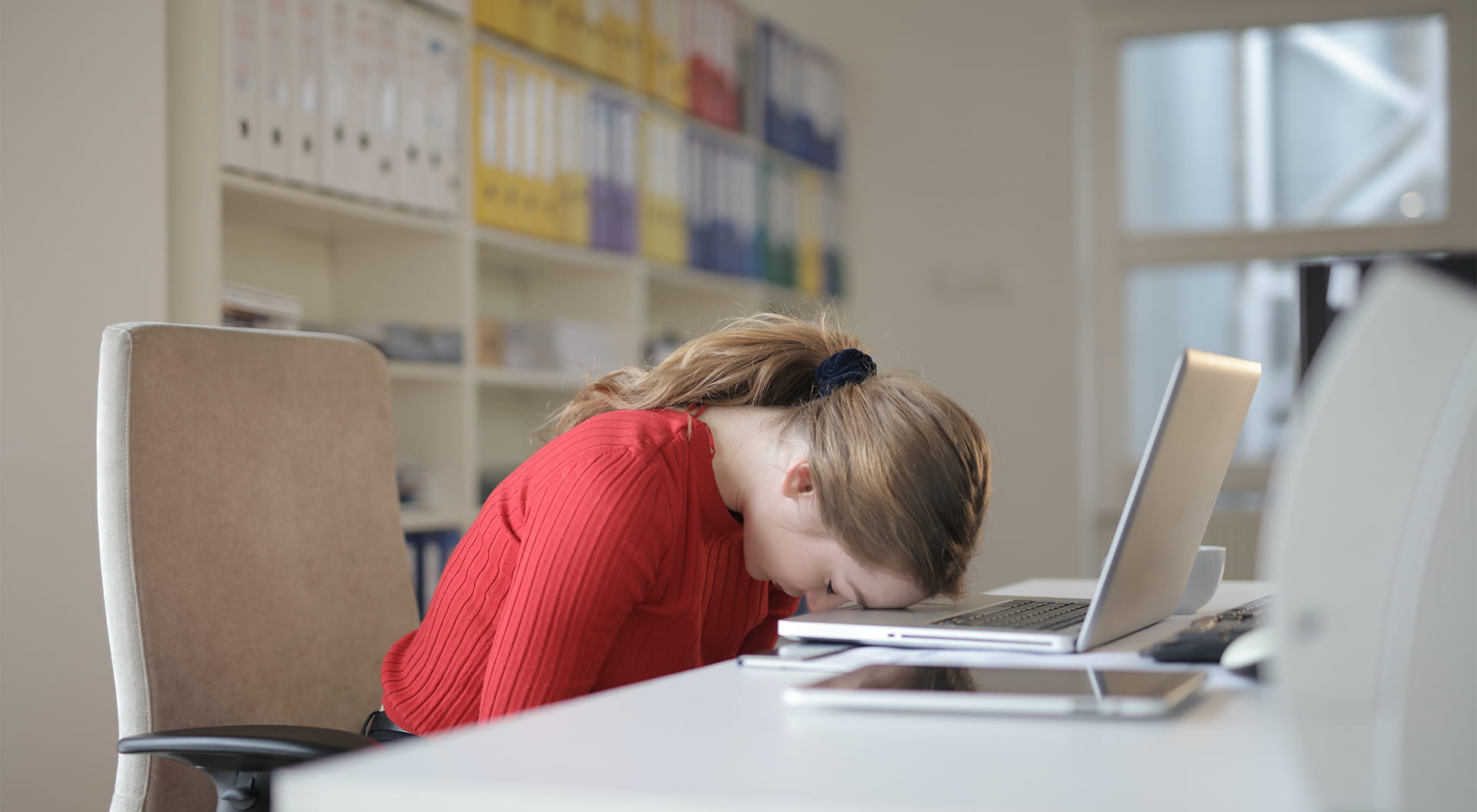 Kvinna vilar huvudet mot en dator på ett skrivbord.