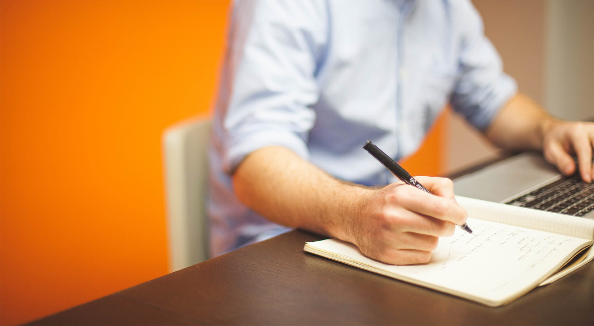 En man sitter vid en dator och antecknar i ett block